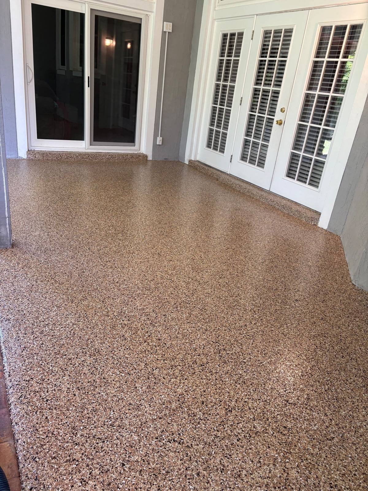Tan and brown flake floor on a covered lanai beside white French doors