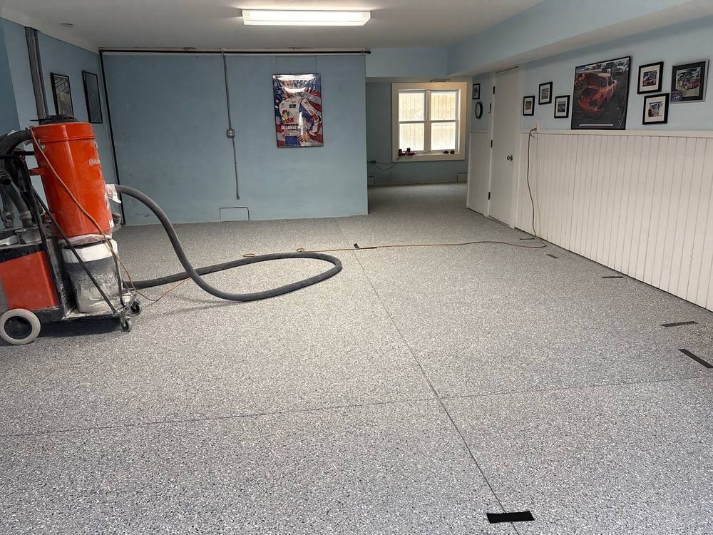 Gray flake floor in a room with light-blue walls, with a floor vacuum and hose beside it