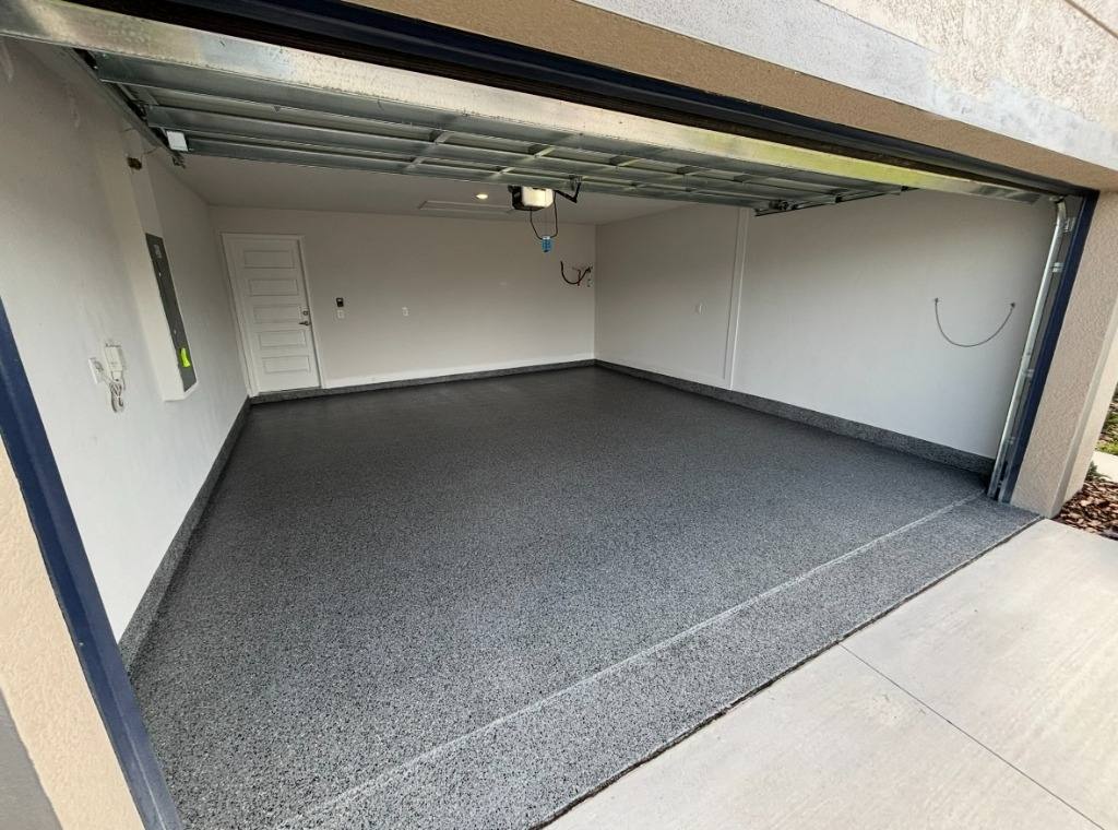 Gray flake floor in an empty two-car garage, seen from the driveway with the door up